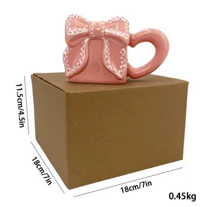 Dettaglio di una tazza in ceramica rosa con fiocco 3D su scatola regalo in kraft