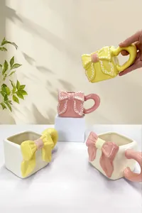 Dettaglio del design con fiocco 3D su tazze in ceramica colorate in giallo e rosa
