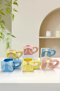 Set di tazze in ceramica pastello con fiocco a rilievo e grandi manici su basi bianche