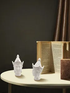 Close-up of two white resin Buddha head statues with intricate headgear on a round table