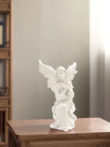 Macro detail of a kneeling white angel girl statue with wings on a wooden surface