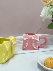 Dettaglio di tazze da caffè in ceramica con fiocco 3D e cucchiaino dorato coordinato