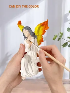 Close-up of hand painting a white resin angel figurine with vibrant orange wings