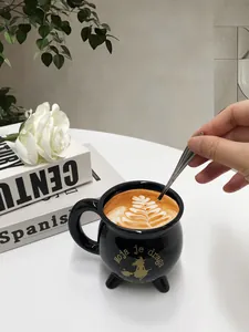 Detail einer Hexenkessel-Tasse mit goldenem Druck und drei Füßen auf weißem Tisch