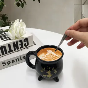 Schwarze Hexenkessel-Kaffeetasse aus Keramik mit goldenem Hexendesign auf weißem Grund