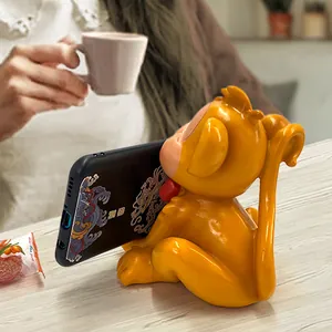 Creative orange monkey resin phone stand holding a smartphone on a wooden desk setup