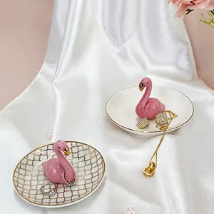 Detailed view of pink ceramic flamingo jewelry dishes on white silk with pearls
