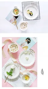Close-up of cream ceramic jewelry dish with gold dot rim and crown handle details