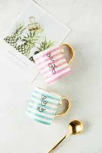 Detail of pink and blue striped ceramic mugs with gold handles and baby lettering