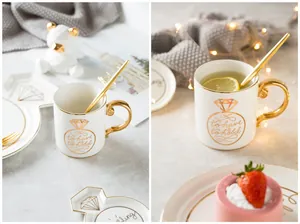 Close-up of white ceramic mug set with gold handle and to have and to hold engraving