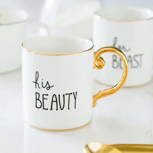 Close-up of ceramic mugs with gold handles and 'his BEAUTY' 'her BEAST' artistic text