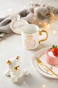 Detail of luxury ceramic gift set with gold-rimmed white mug and decorative ring tray