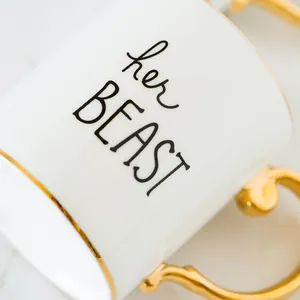 Detail of white ceramic mug with gold-plated handle and elegant 'her BEAST' art print