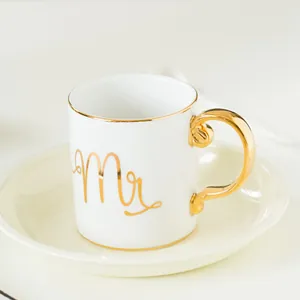 Detail of white ceramic mug with gold rim, Mr lettering and elegant gold handle