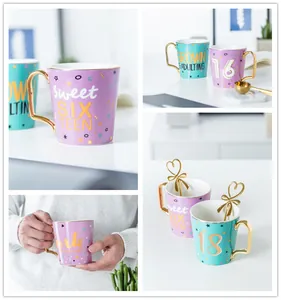 Dettaglio di tazze di compleanno in ceramica con manici dorati e cucchiai a cuore