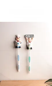 Detail view of cartoon chef wall hooks holding toothbrushes against white bathroom tiles