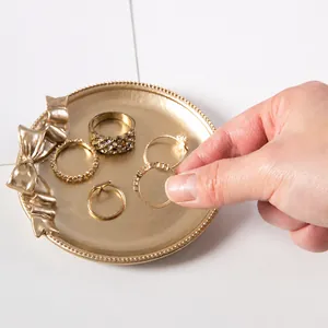 Golden bow jewelry tray with five minimalist and zircon-encrusted rings set on white base