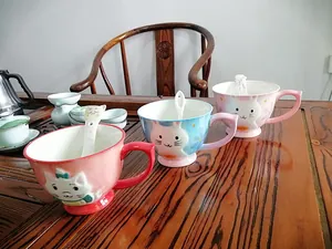 Close-up of ceramic mugs with cute animal relief and matching spoons on a wooden table