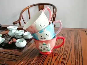 Close-up of stacked ceramic mugs featuring embossed cartoon cat designs and smooth glaze