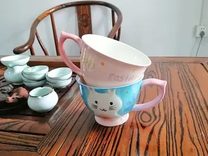Detail of pink and blue ceramic mugs featuring a unique curved handle and cartoon cat motif