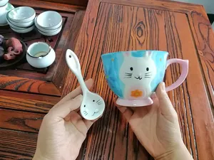 Detail view of cartoon ceramic mug set with spoon held in hands over a wooden tray