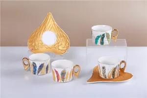 Vue détaillée d'une tasse à café en céramique avec anses dorées en forme d'ailes et soucoupe