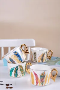 Détail de tasses en céramique avec motifs plumes de paon et anses ailes d'ange dorées