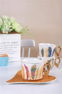 Vue détaillée d'une tasse à café en céramique au motif plume et anse dorée sculptée