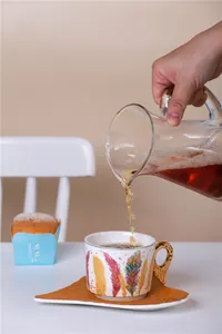 Gros plan du thé versé dans une tasse en céramique à motif de plumes avec sa soucoupe
