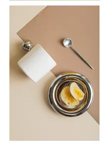 Detail view of a white ceramic mug with silver sphere handle and polished metal saucer