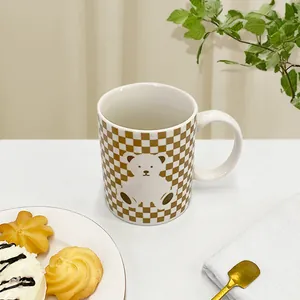 Close-up of ceramic mug with brown checkerboard pattern and cute white bear in a tea setting