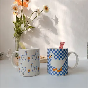 Close-up of ceramic mugs with cute duck patterns and matching spoons on a sunlit table