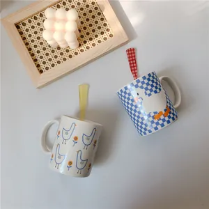 Detail of ceramic duck mugs with matching checkered spoons on a cozy white desk setup