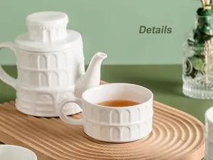 Macro detail of white ceramic teapot and cup with Roman arch relief on wooden tray