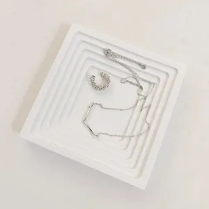 Elegant silver necklace and ear cuff set displayed on a white marble prop pedestal