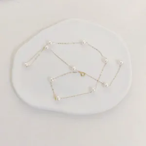 Detail view of a dainty gold pearl necklace on a white minimalist matte resin tray