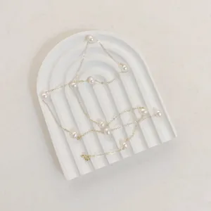 Detail of star-style pearl necklace displayed on a white arched striped resin tray