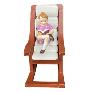 Close-up of resin dollhouse miniature girl reading on a brown rocking chair