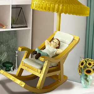 Miniature resin boy relaxing in a golden rocking chair with a yellow sun umbrella for garden