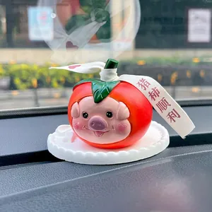 Close-up of resin pig persimmon car ornament with red ribbon on white base