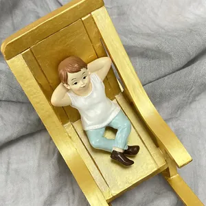 Detail of miniature boy figurine with golden rocking chair for dollhouse garden decor