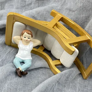 Top view of a resin miniature boy figurine lounging on a gold and white garden bench