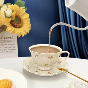 Macro view of floral ceramic coffee cup with gold rim being filled with milk tea