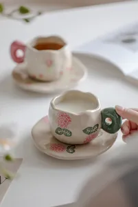 Detail of hand-painted ceramic coffee cup and saucer set with floral and berry motifs