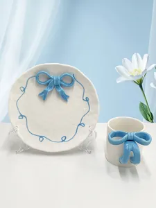 Dettaglio set colazione in ceramica con fiocco blu 3D e linee ondulate dipinte a mano