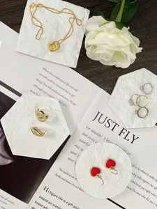 Primer plano de collar dorado y pendientes de corazón en bandejas de mármol con rosa