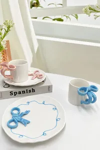 Dettaglio di tazzina da caffè in ceramica con manico a fiocco 3D e bordo ondulato