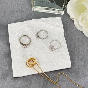 Vista detallada de anillos de lujo y collar sobre una bandeja blanca con textura