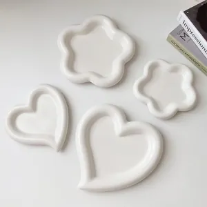 Vista dall'alto di piatti in ceramica color crema a forma di cuore e fiore su sfondo bianco