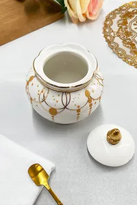 Detail of Nordic white ceramic sugar jar with gold trim patterns and golden spoon